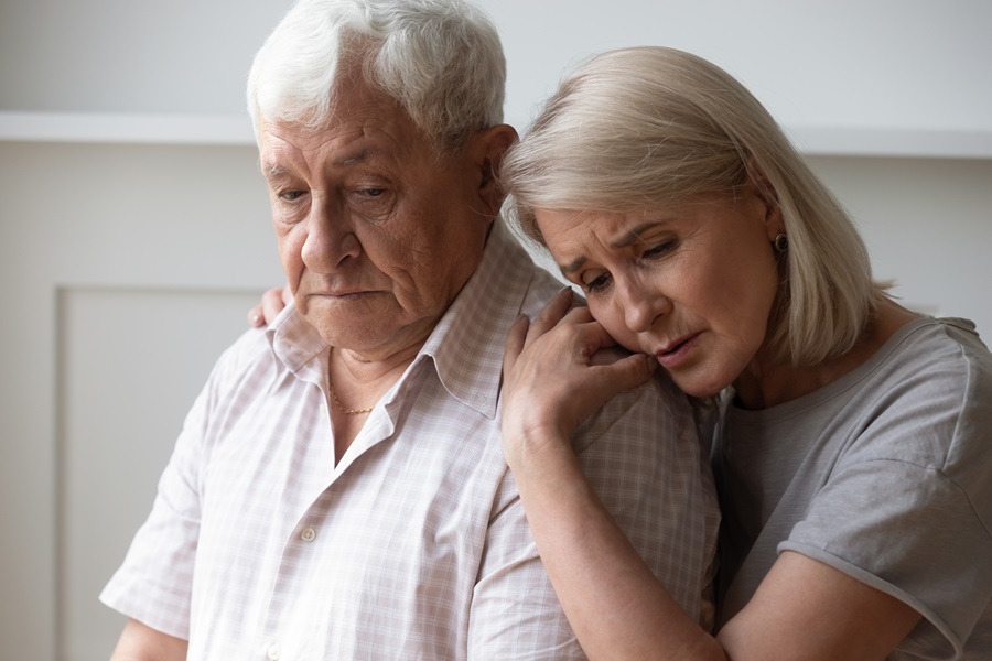 Älterer Mann schaut traurig und wird von hinten von einer jungen Frau umarmt