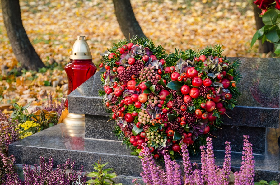 Blumengesteck in Herzform mit roten Zieräpfeln, das an einem Grabstein lehnt