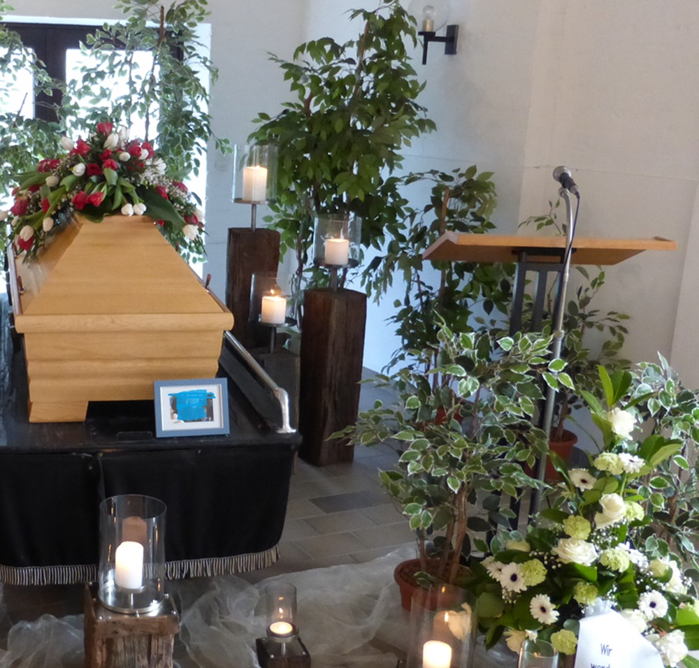 Sarg mit Blumenschmuck und daneben ein Redner-Pult mit Mikrofon in einer Kapelle